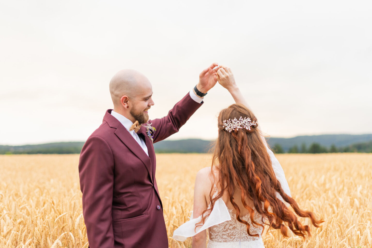 Hochzeitspaar auf einem weiten Feld sind am Tanzen. Bräutigam in einem weinroten Anzug bestaunt seine Braut.