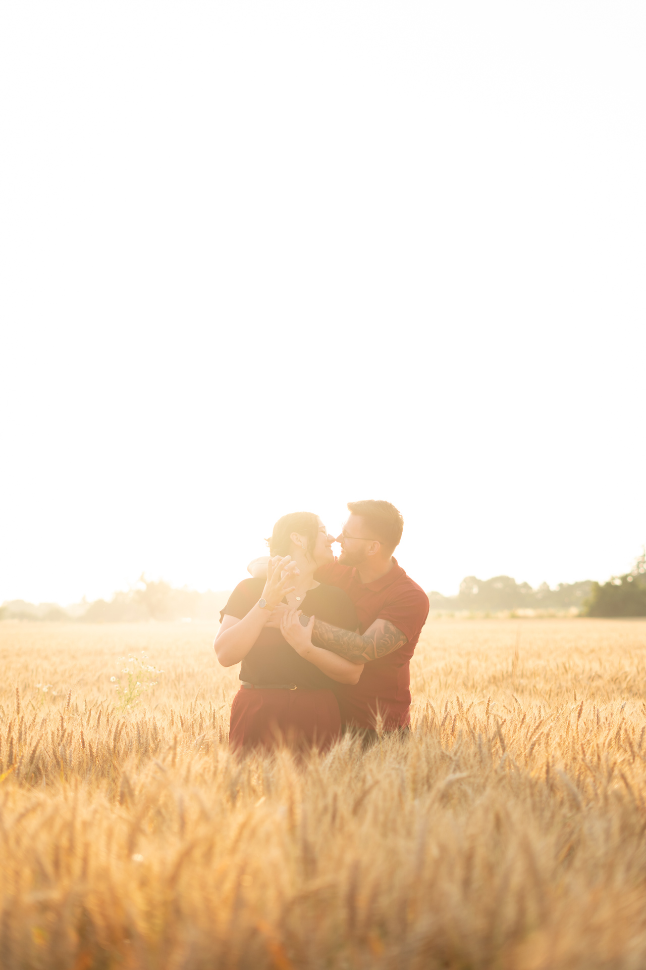 Verlobtes Paar auf Kornfeld küsst sich beim Sonnenuntergang, aufgenommen von Fotograf Jonathan Gäßler.