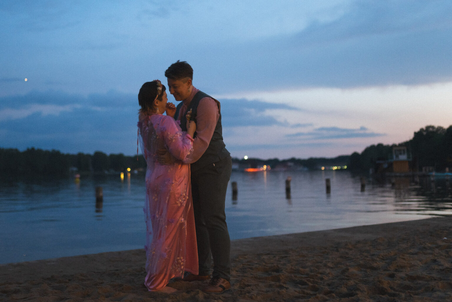 Hochzeitspaar, zwei Frauen, die sich vor einem See am Strand einen Kuss geben von Hochzeitsfotograf in Offenburg Jonathan Gäßler festgehalten.